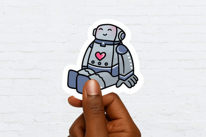 Hand holding a sticker of a robot with a heart on a white brick wall background