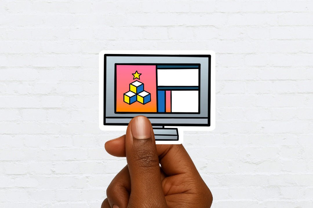 Hand holding a sticker of a computer monitor with colorful graphics against a white brick wall.