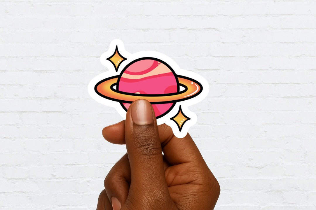Hand holding a colorful planet sticker against a white brick wall background