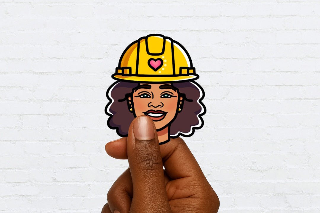 Hand holding a sticker of a woman wearing a yellow hard hat with a heart on a white brick wall background.